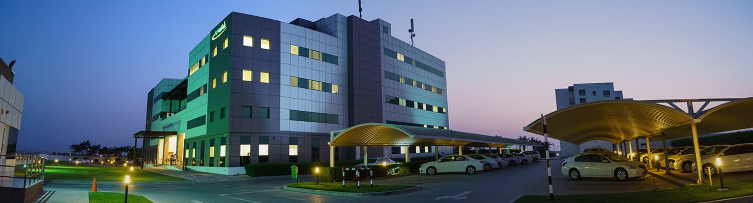 An office building lit at dusk, with a covered car park in front of it