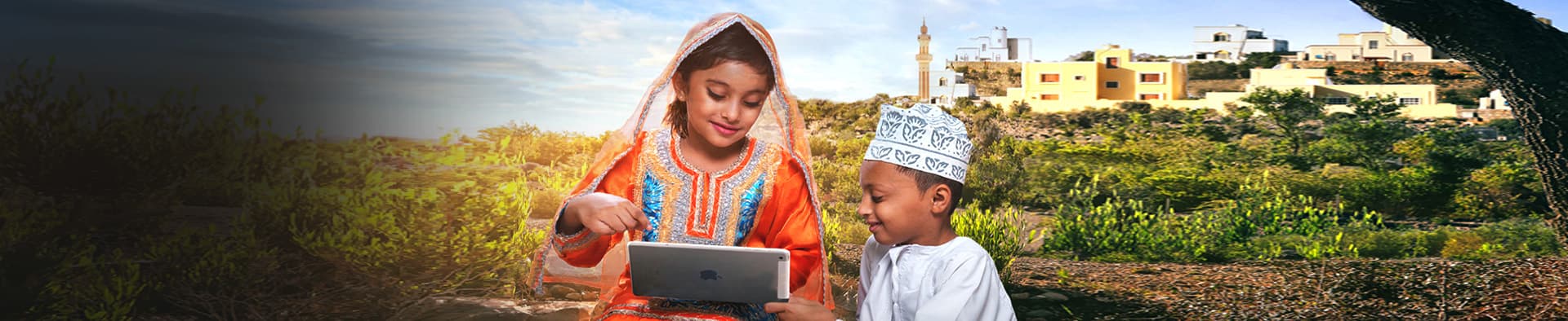 A girl and a boy in traditional Omani dress using a tablet outdoors